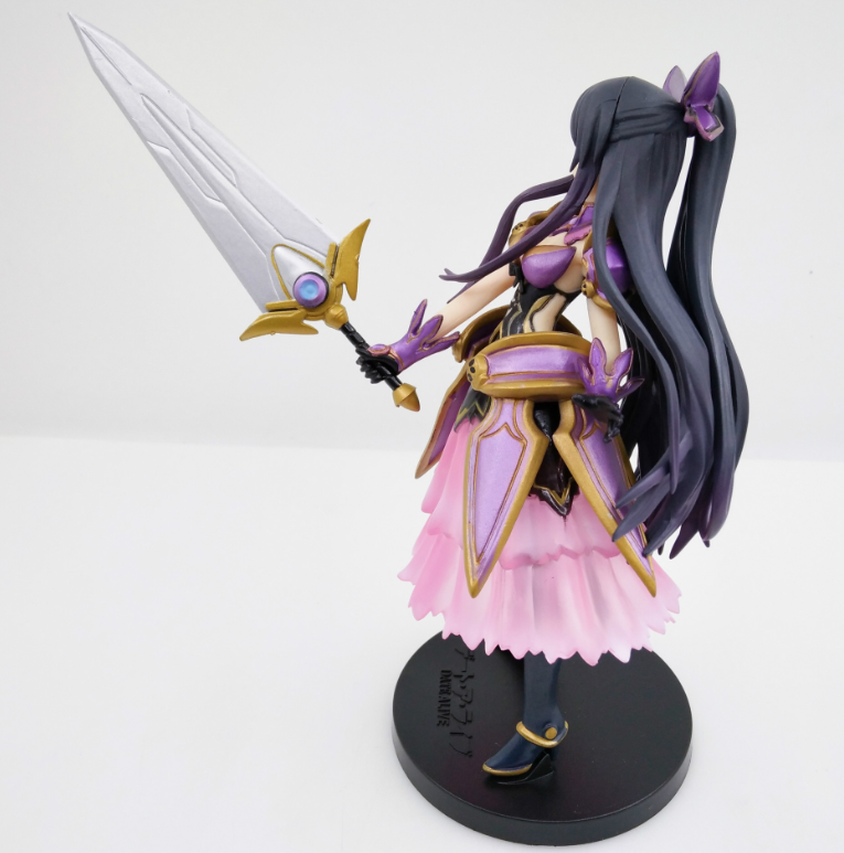 Figurine of a character with long dark hair, purple accents, and a pink dress holding a sword on a white background.